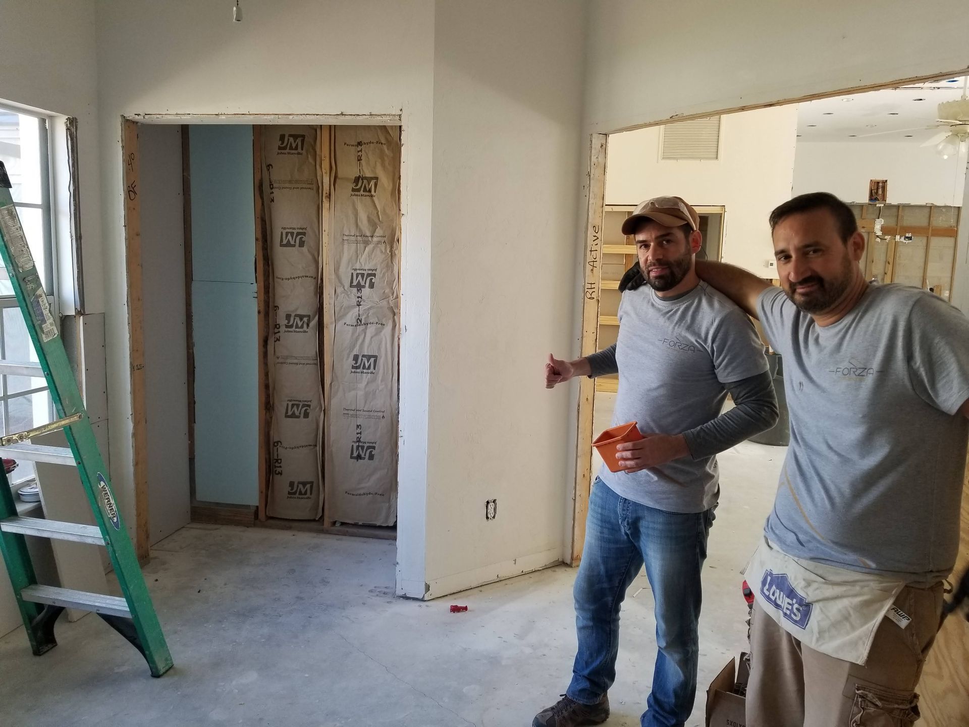 Two men are standing in a room with a ladder in the background.