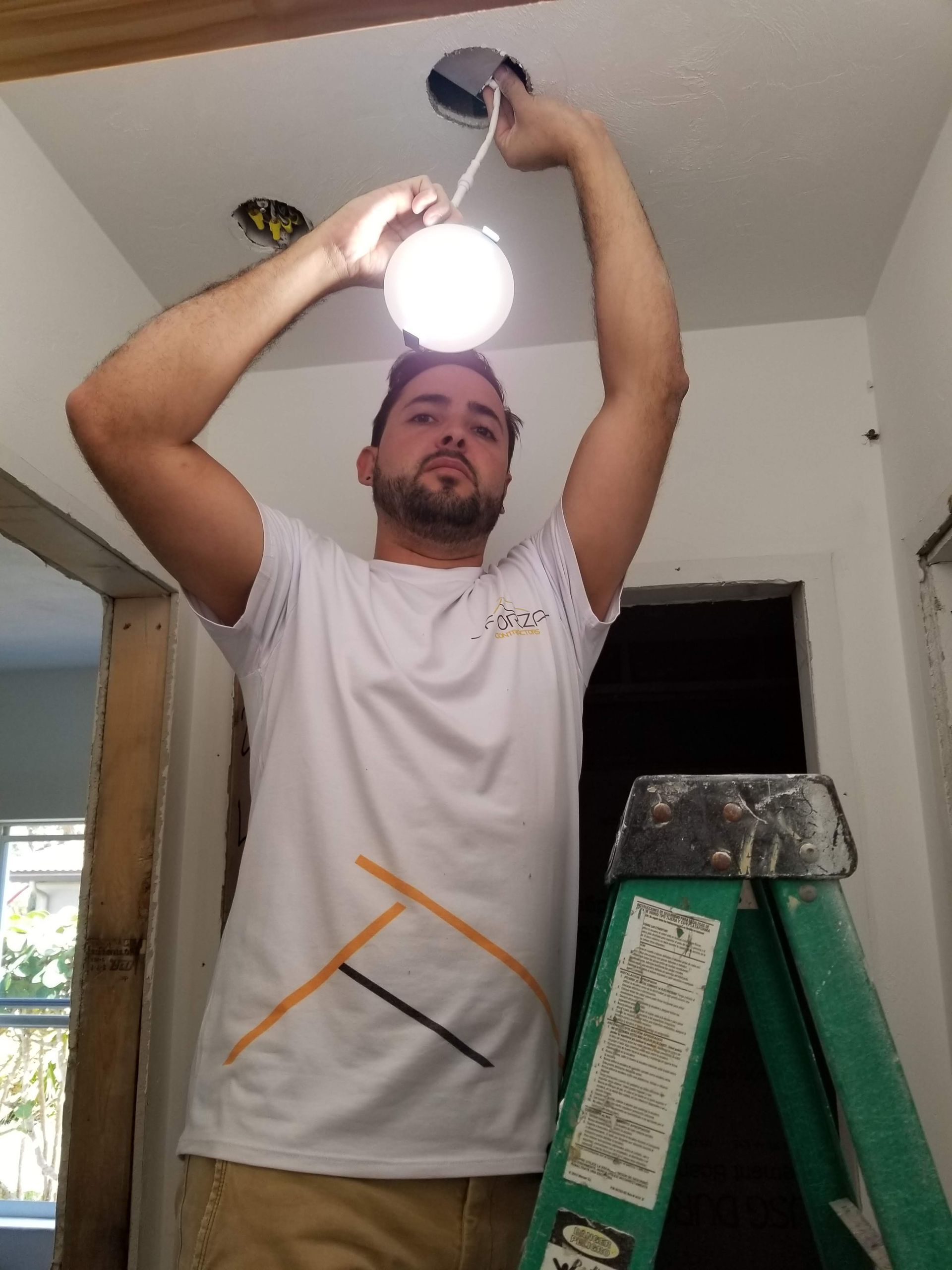 A man is standing on a ladder fixing a light bulb