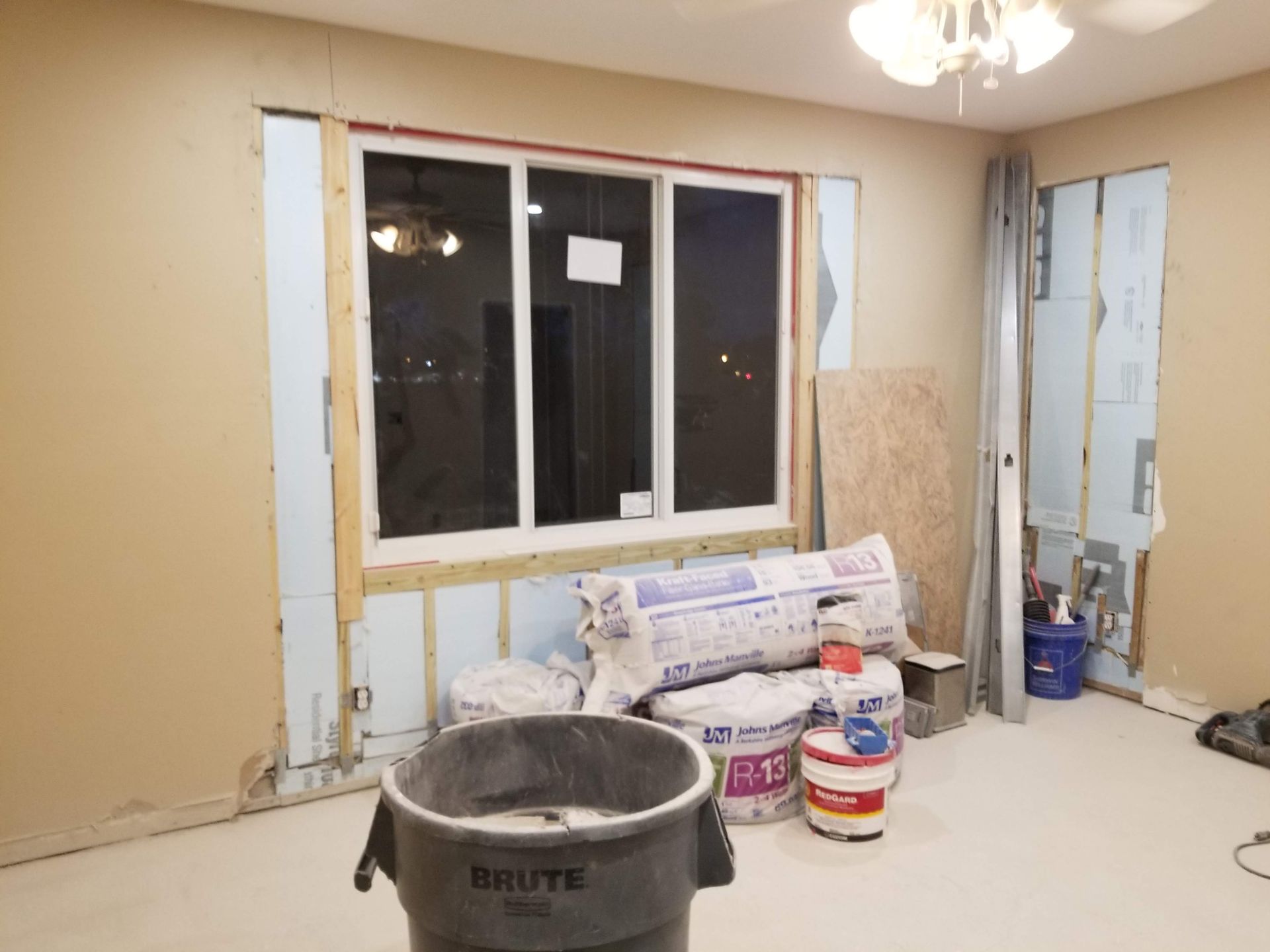 A room under construction with a window and a trash can.