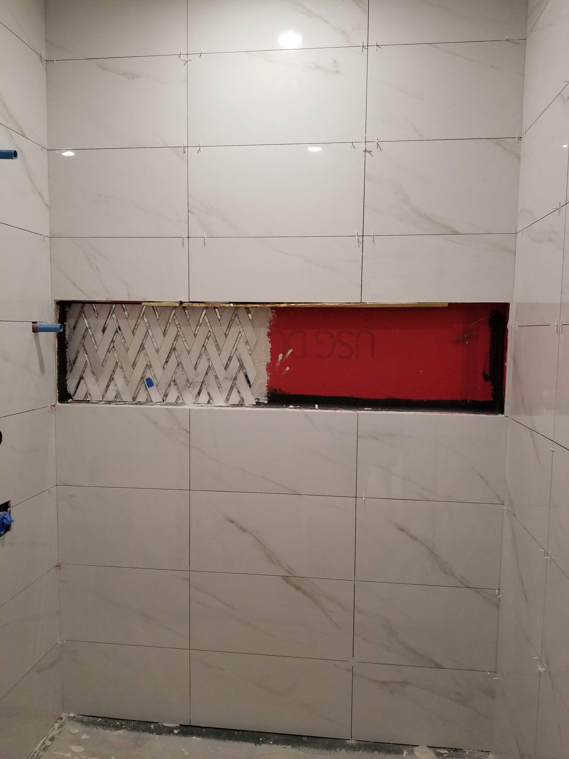 A bathroom with white tiles and a red shelf.