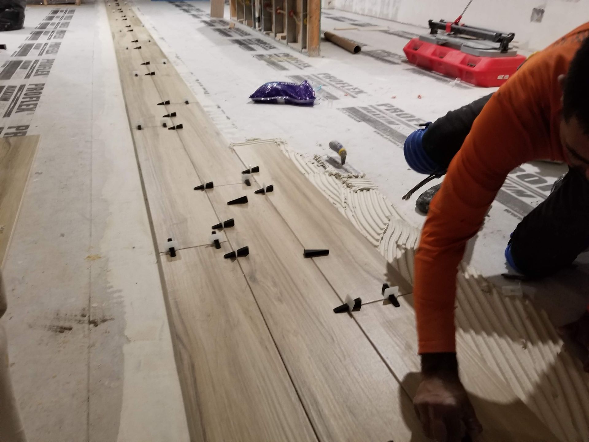 A man is kneeling on a wooden floor with a purple bag on the floor