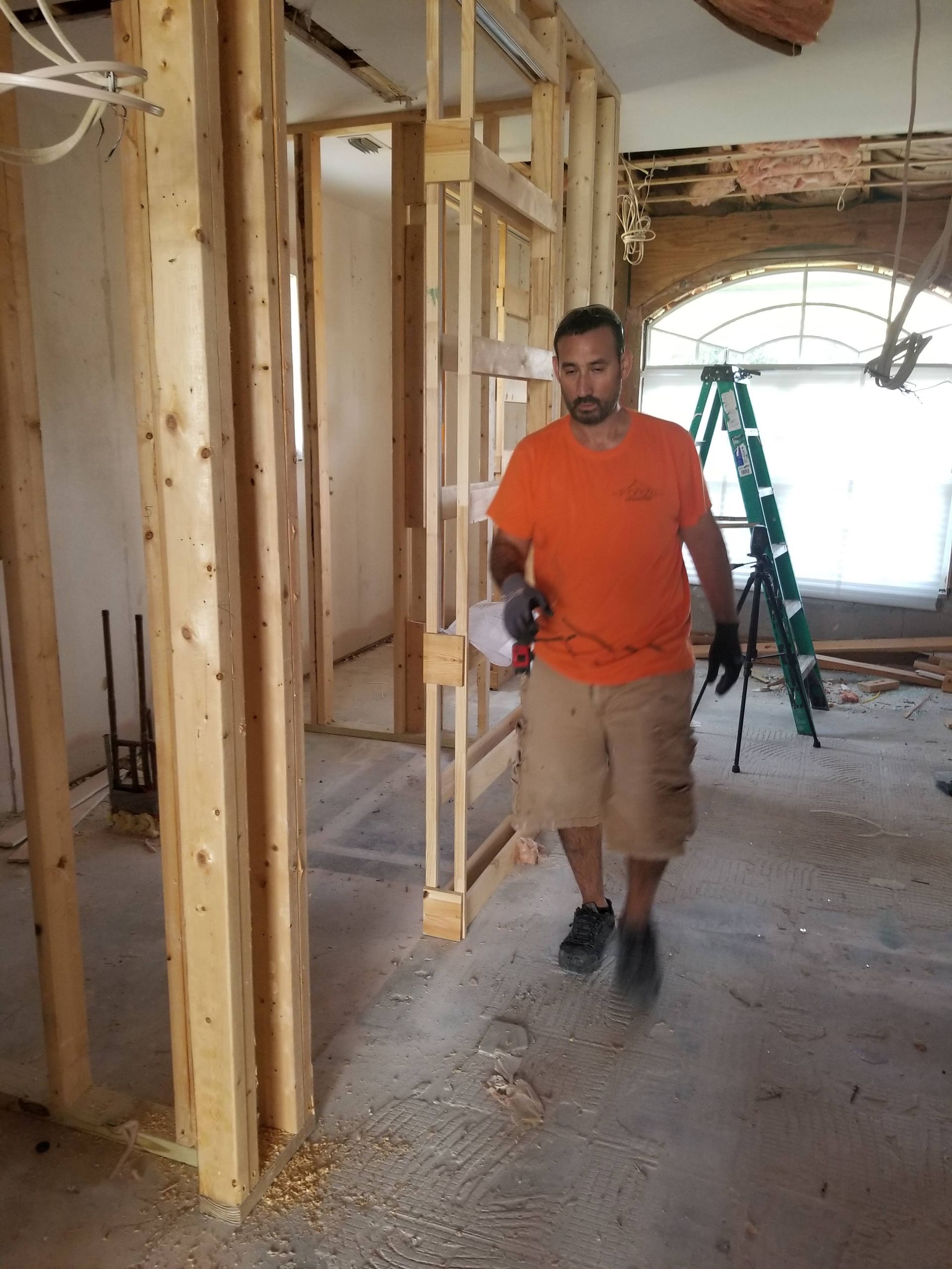 A man in an orange shirt is walking through a room under construction.