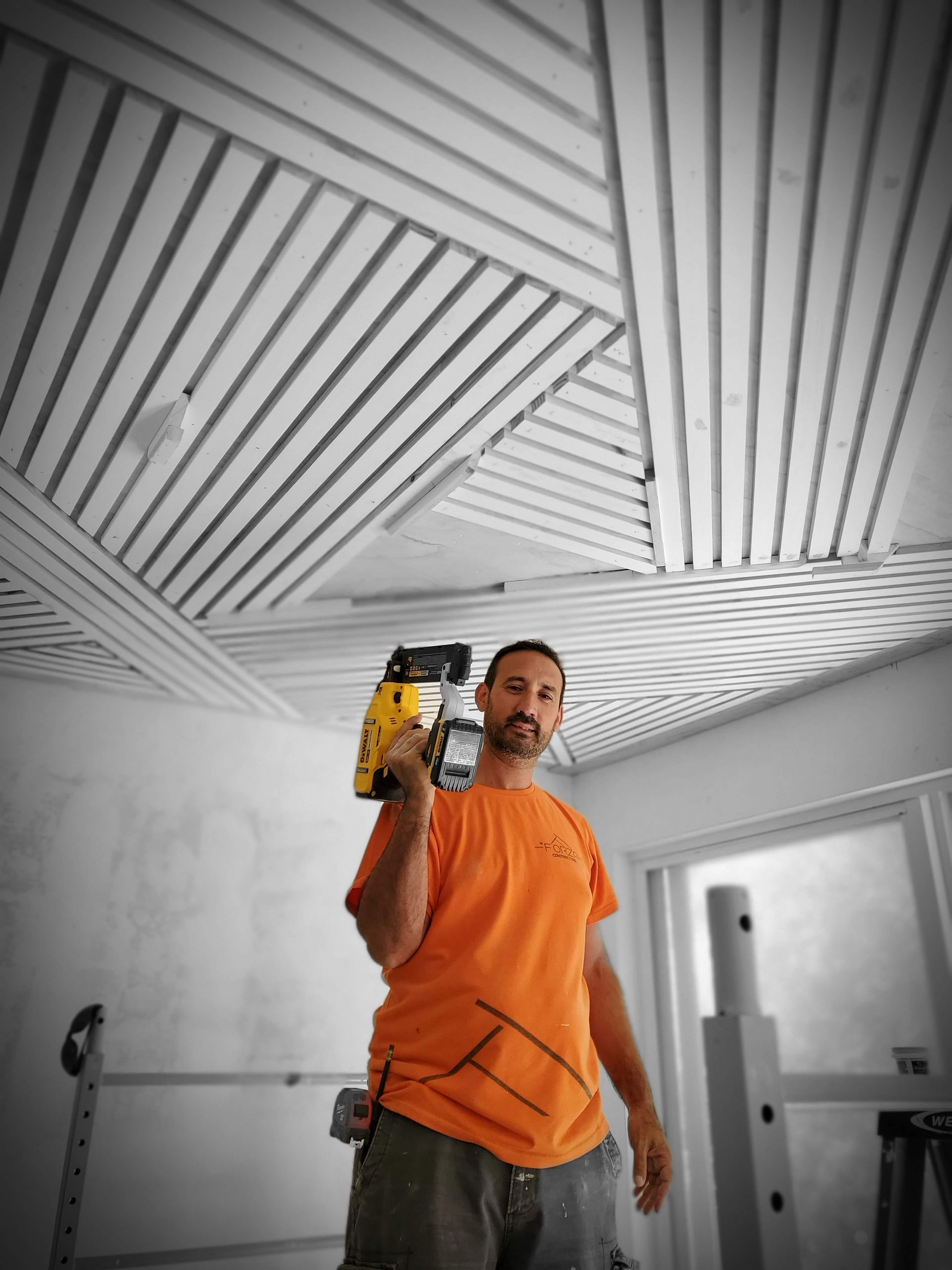 A man in an orange shirt is holding a drill in a room