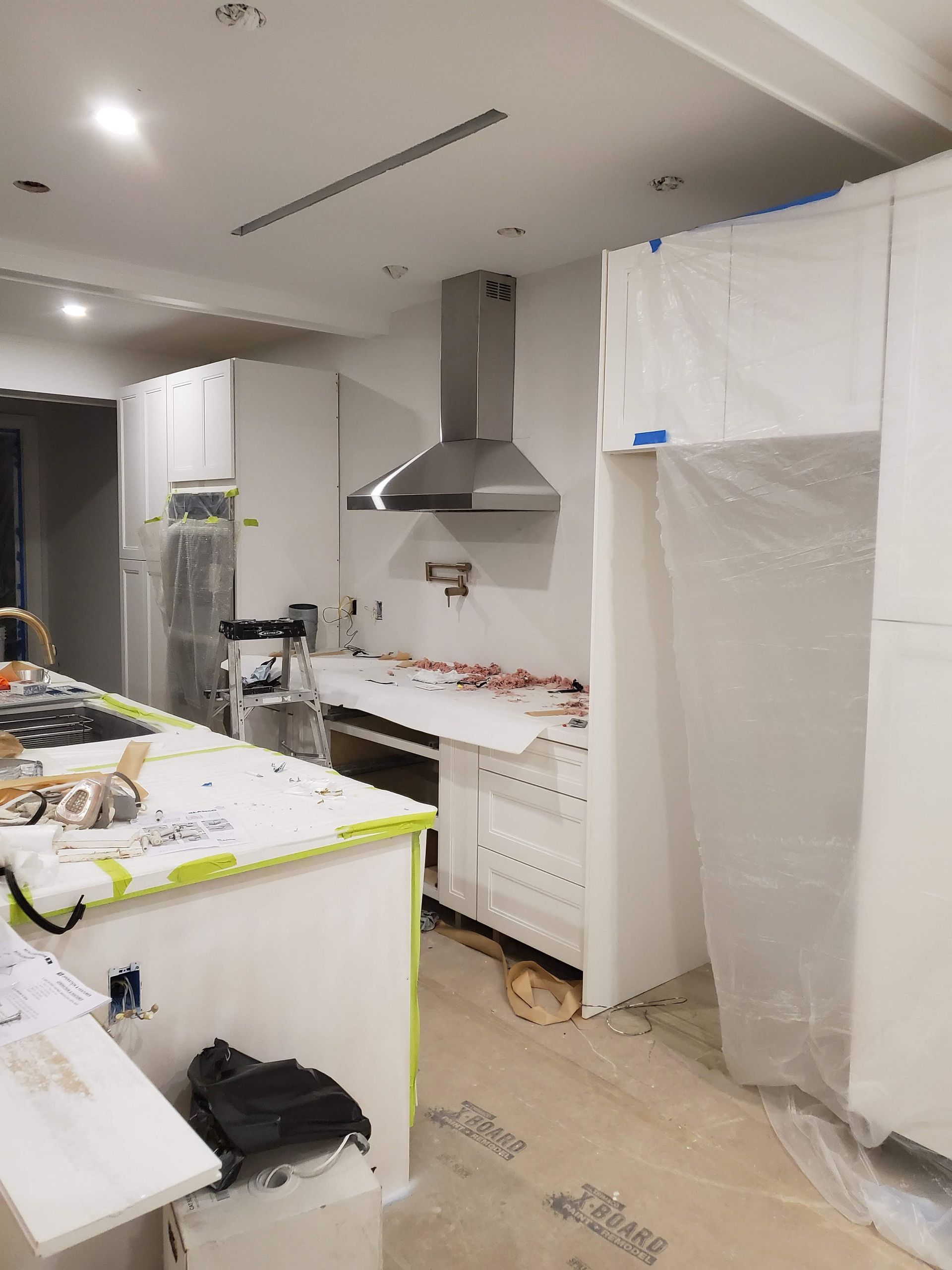 A kitchen under construction with white cabinets and a stainless steel hood.