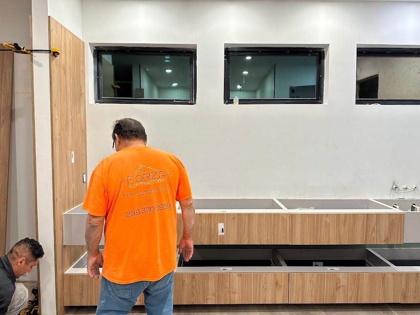 A man in an orange shirt is standing in a kitchen.