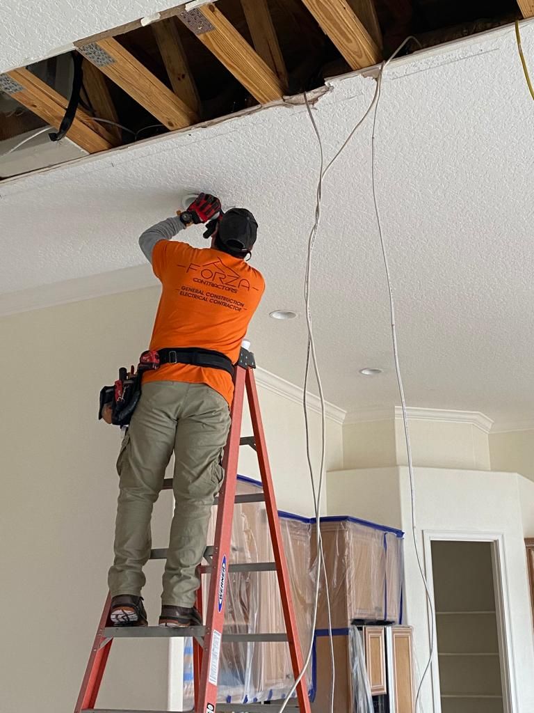 A man is standing on a ladder working on a ceiling.