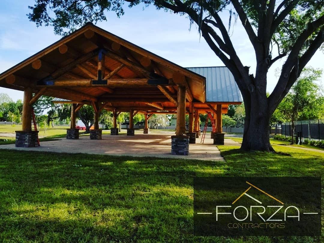 A large wooden pavilion in a park is sponsored by forza construction