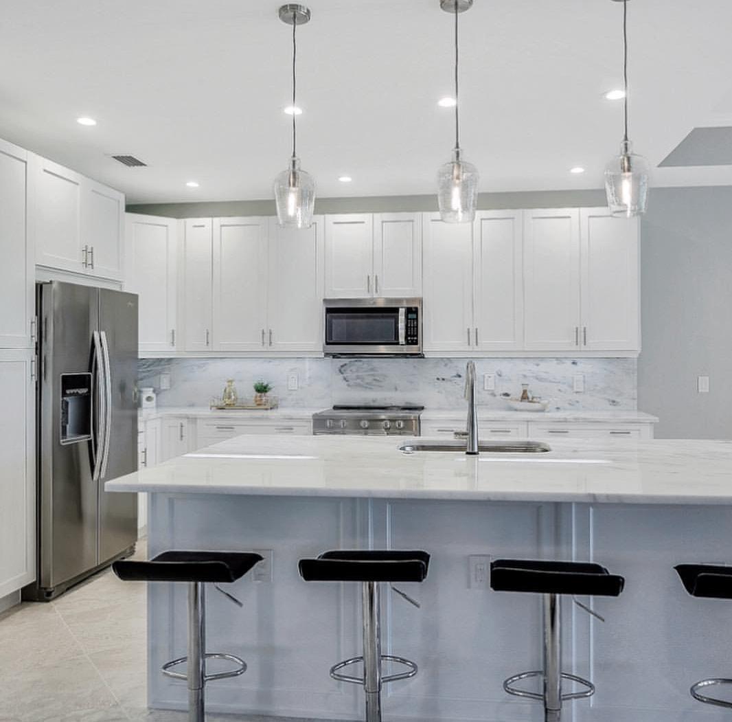 A kitchen with white cabinets , stainless steel appliances , and a large island.