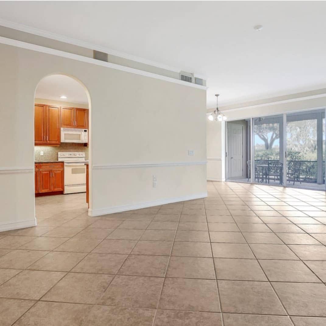 A large empty room with a tiled floor and a kitchen in the background.