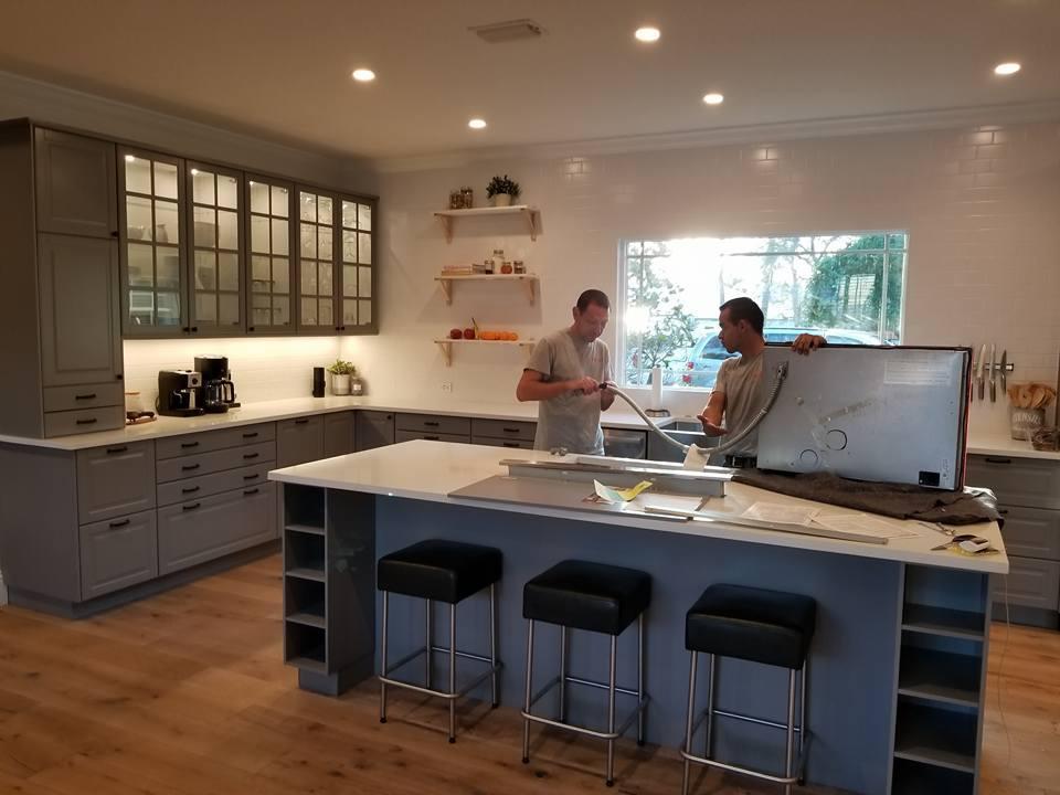 Two men are standing in a kitchen holding a large white board.