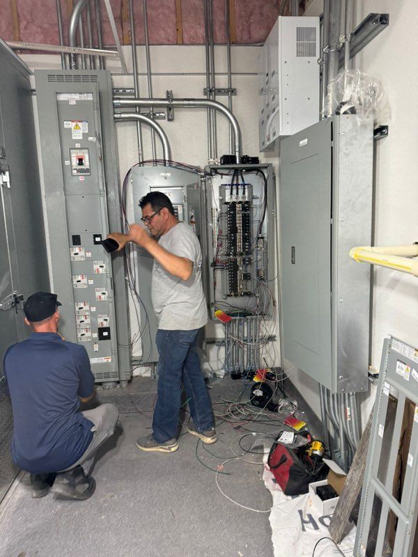 Two men are working on a electrical panel in a room.