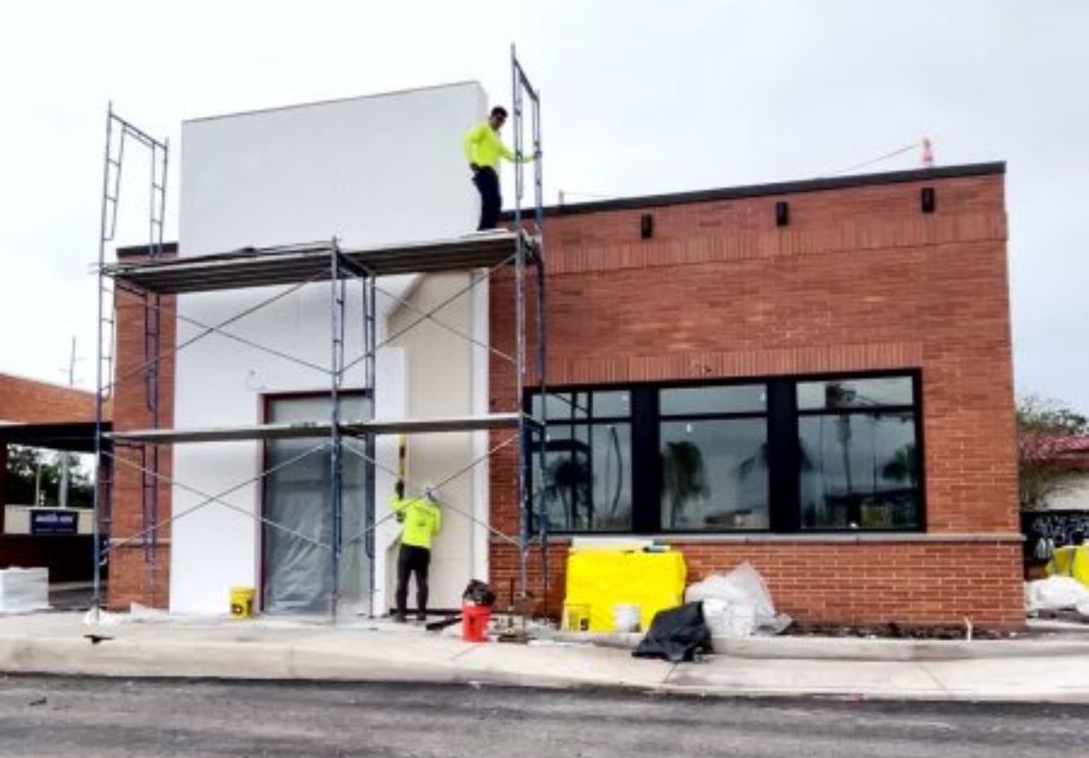Construction workers on scaffolding, painting exterior of brick and white facade building.