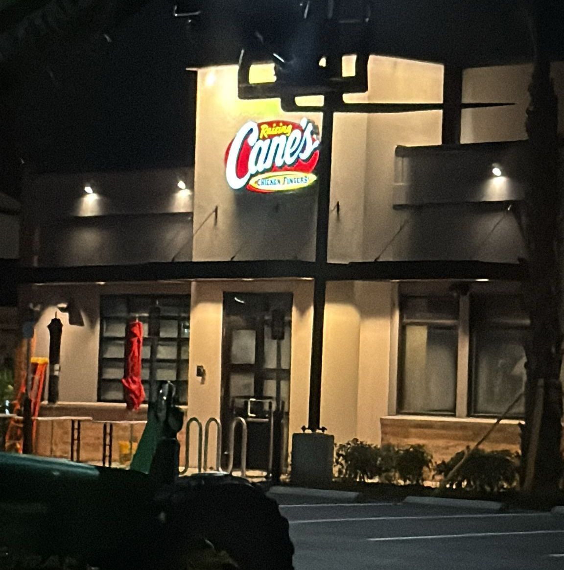 Raising Cane's restaurant at night, illuminated sign, tan building with windows, parking lot, dark sky.
