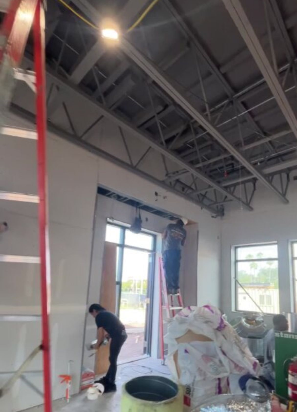 Construction workers inside a building. One on a ladder near an entrance, two others working on walls. Interior view.