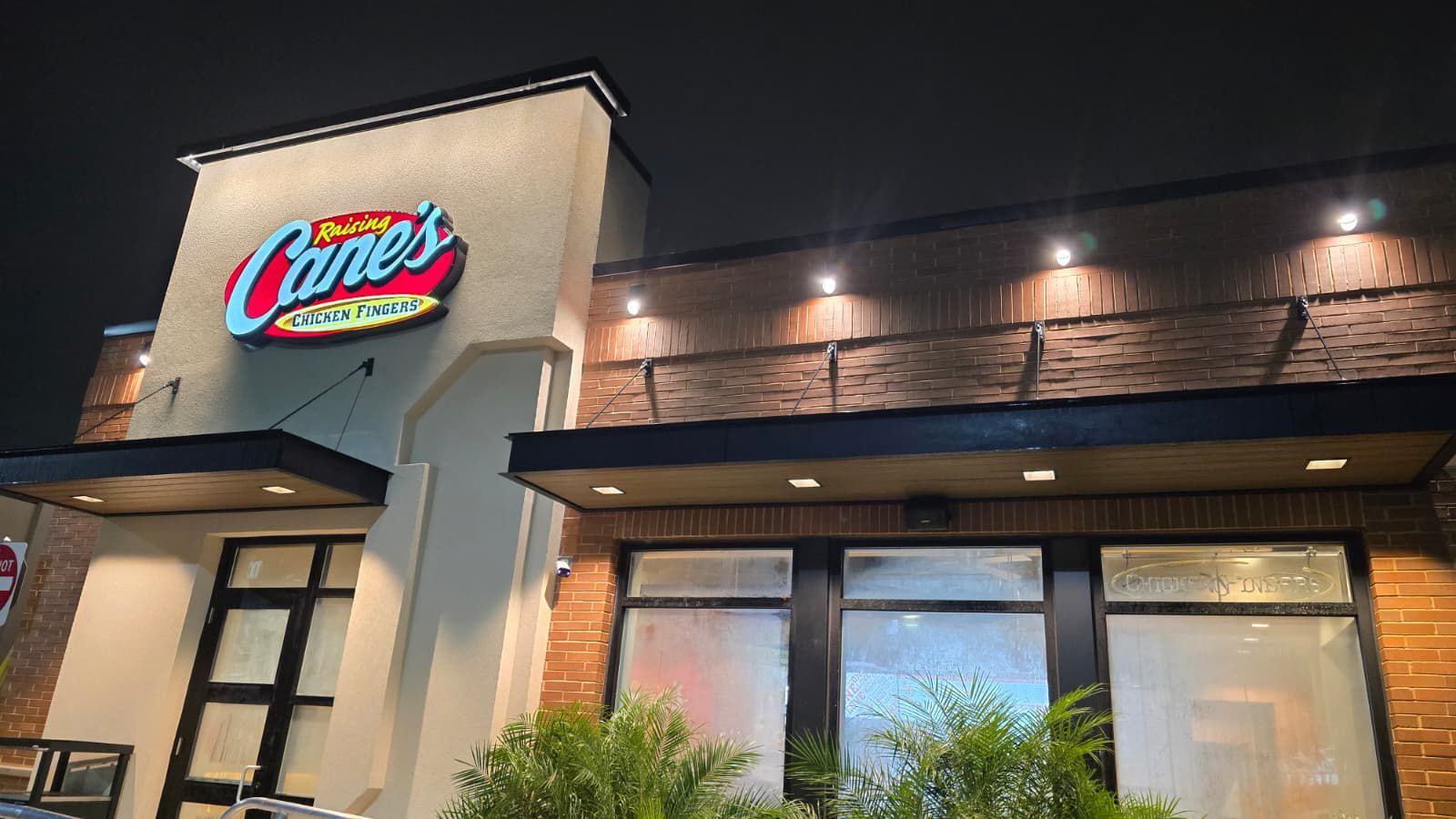 Raising Cane's restaurant exterior at night with illuminated sign and lights above the windows.