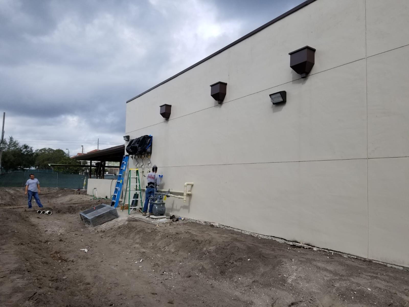 A man is painting the side of a building with a ladder.
