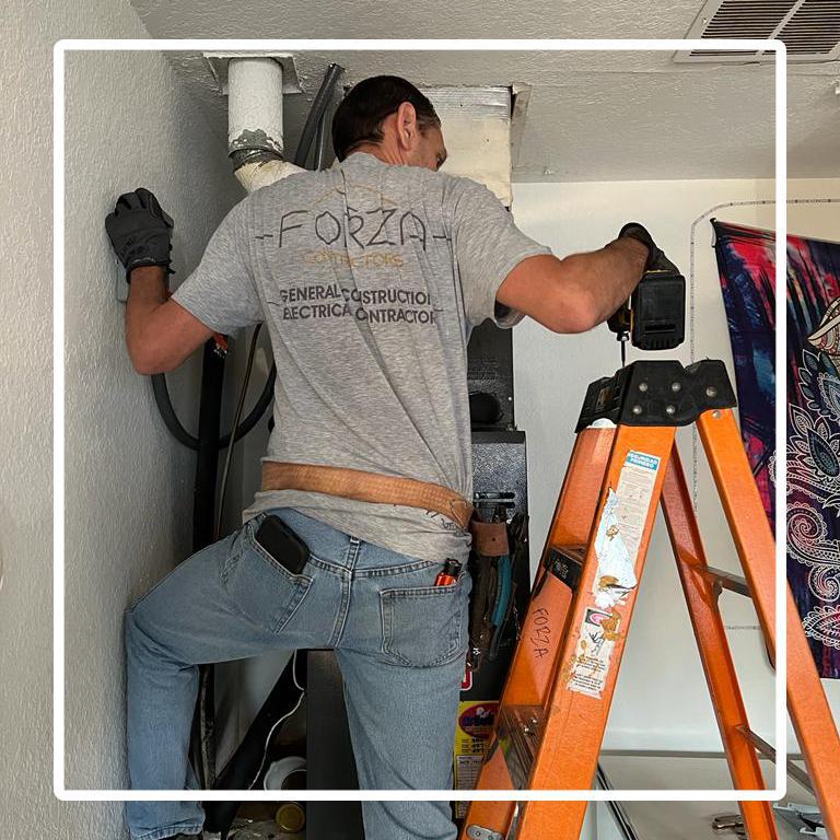 A man is standing on a ladder working on an air conditioner.