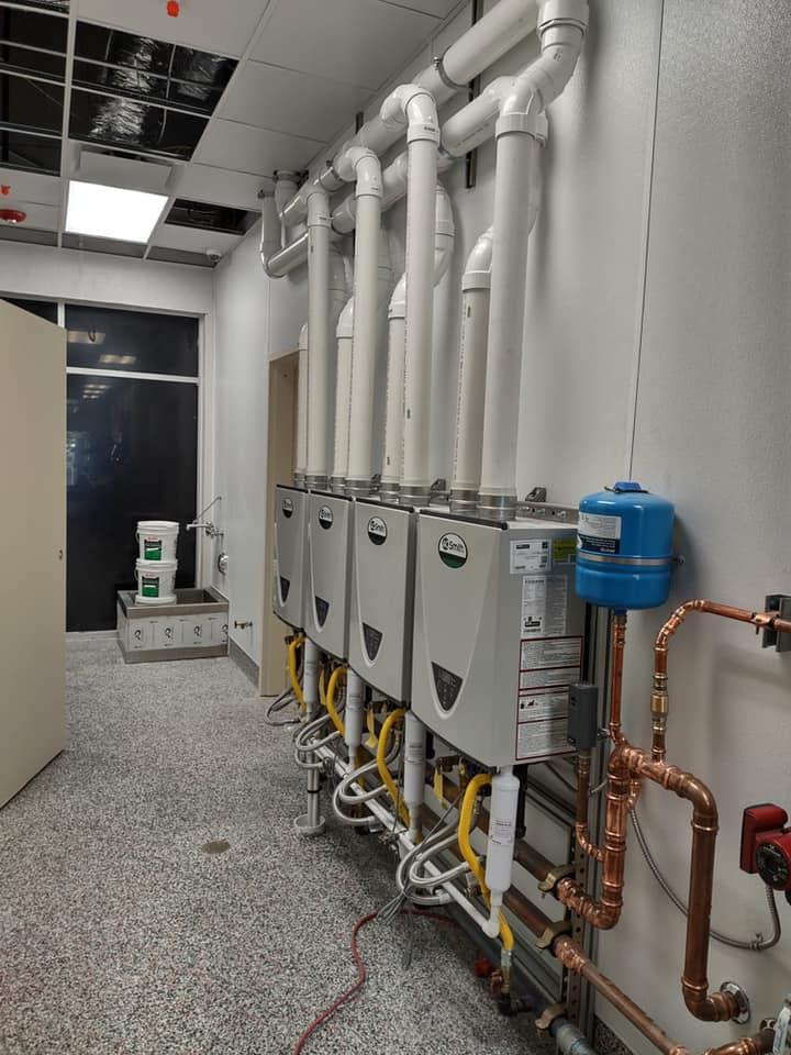 A room with a row of water heaters and pipes on the wall.