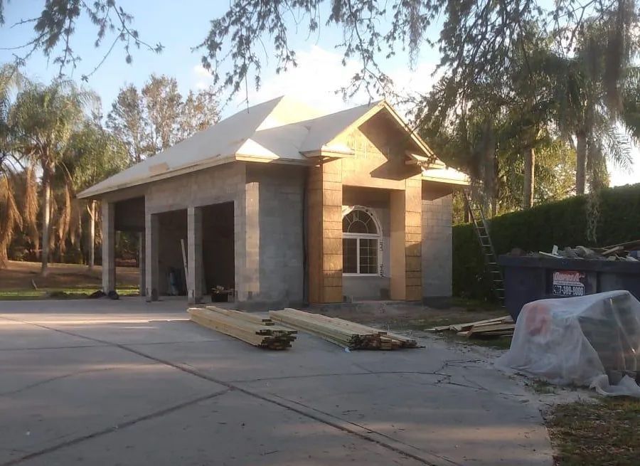 Garage under construction; concrete block structure, wooden roof frame, lumber on driveway.