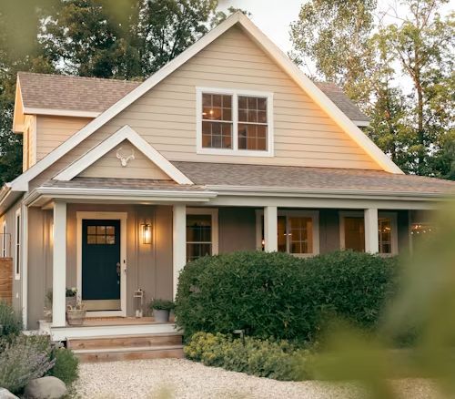 Tan house with dark blue door, white trim, porch, and landscaping.