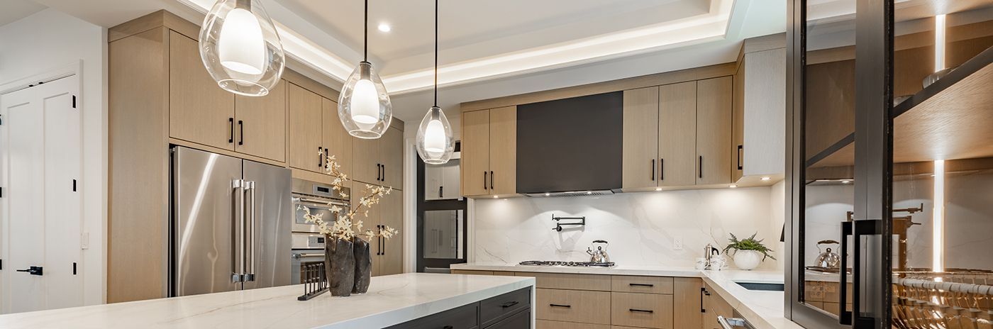 A modern kitchen with light-colored cabinets, a large island, and hanging globe lights.