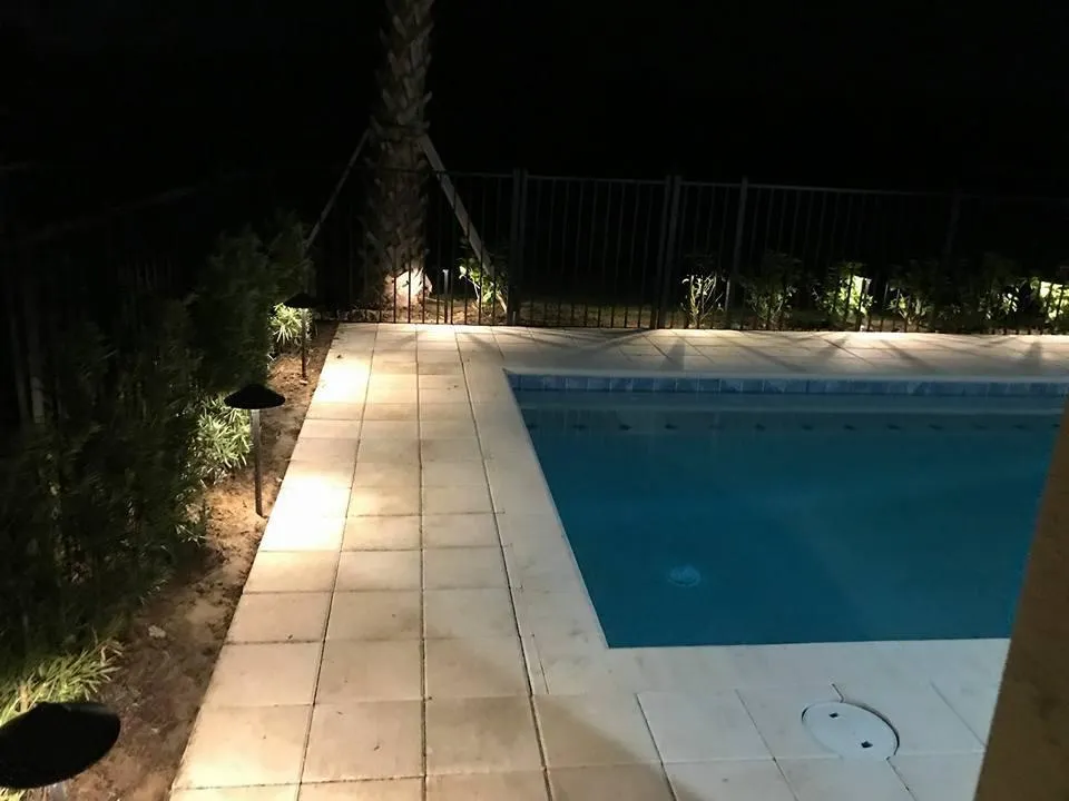 A swimming pool is lit up at night in a backyard.
