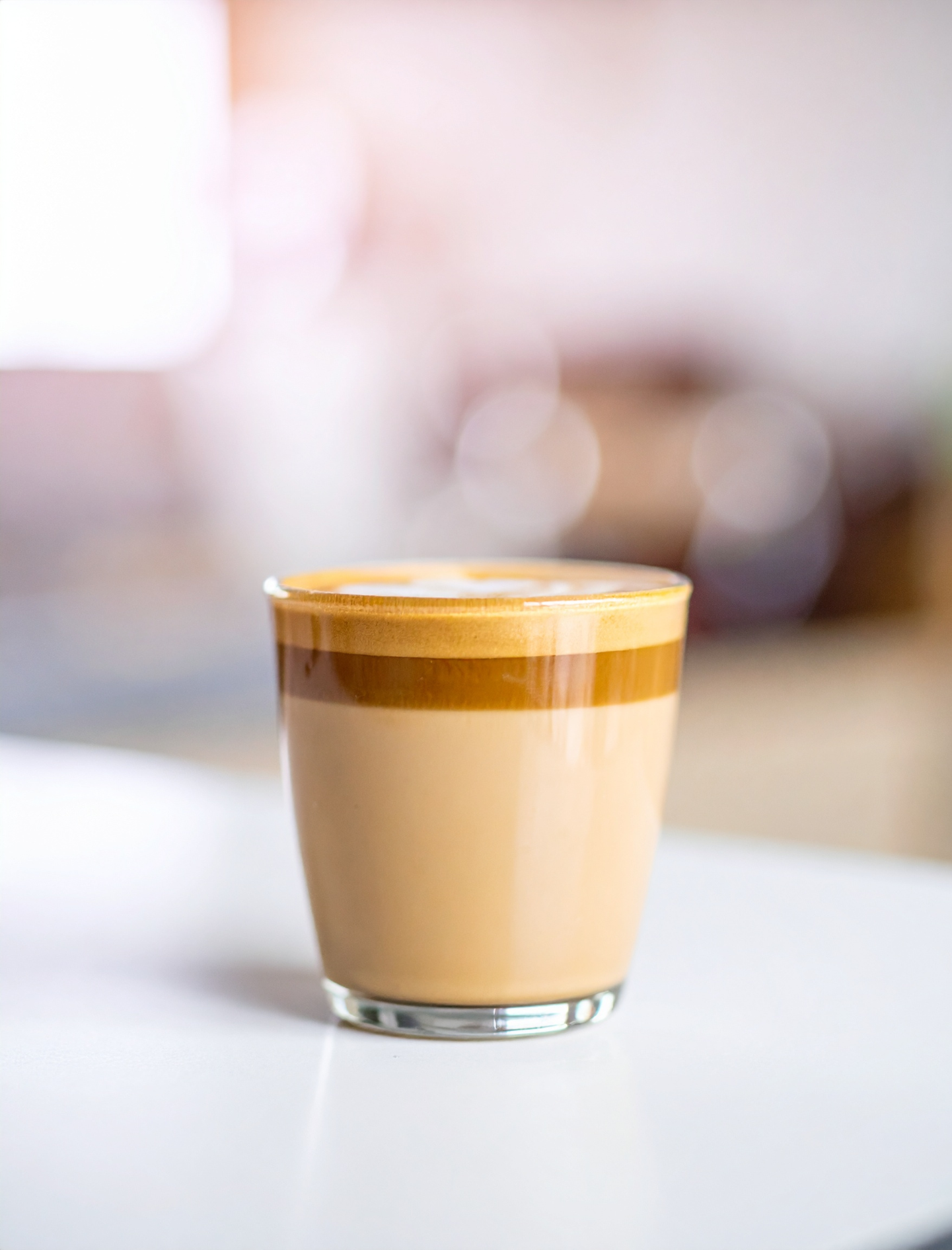 A glass of layered latte on a table, with a blurred café background