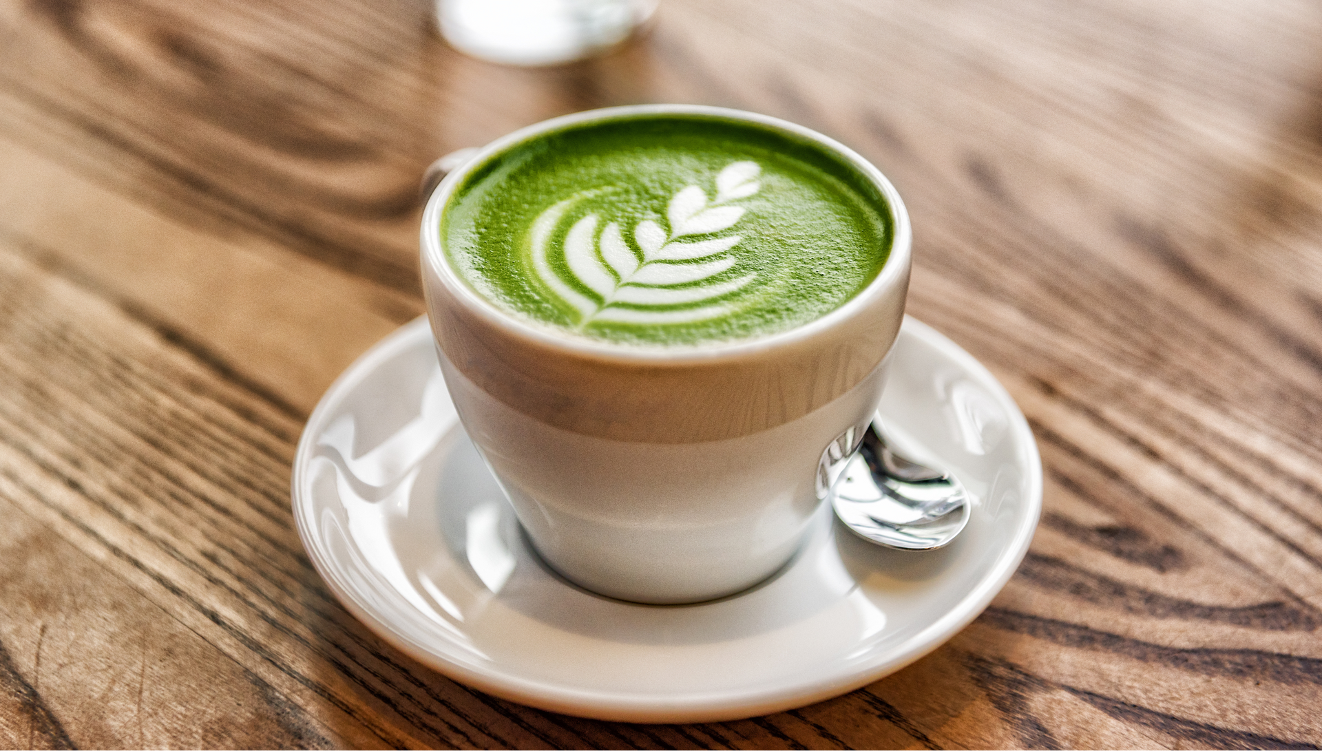 Cup of green latte art on a saucer with a spoon on a wooden table