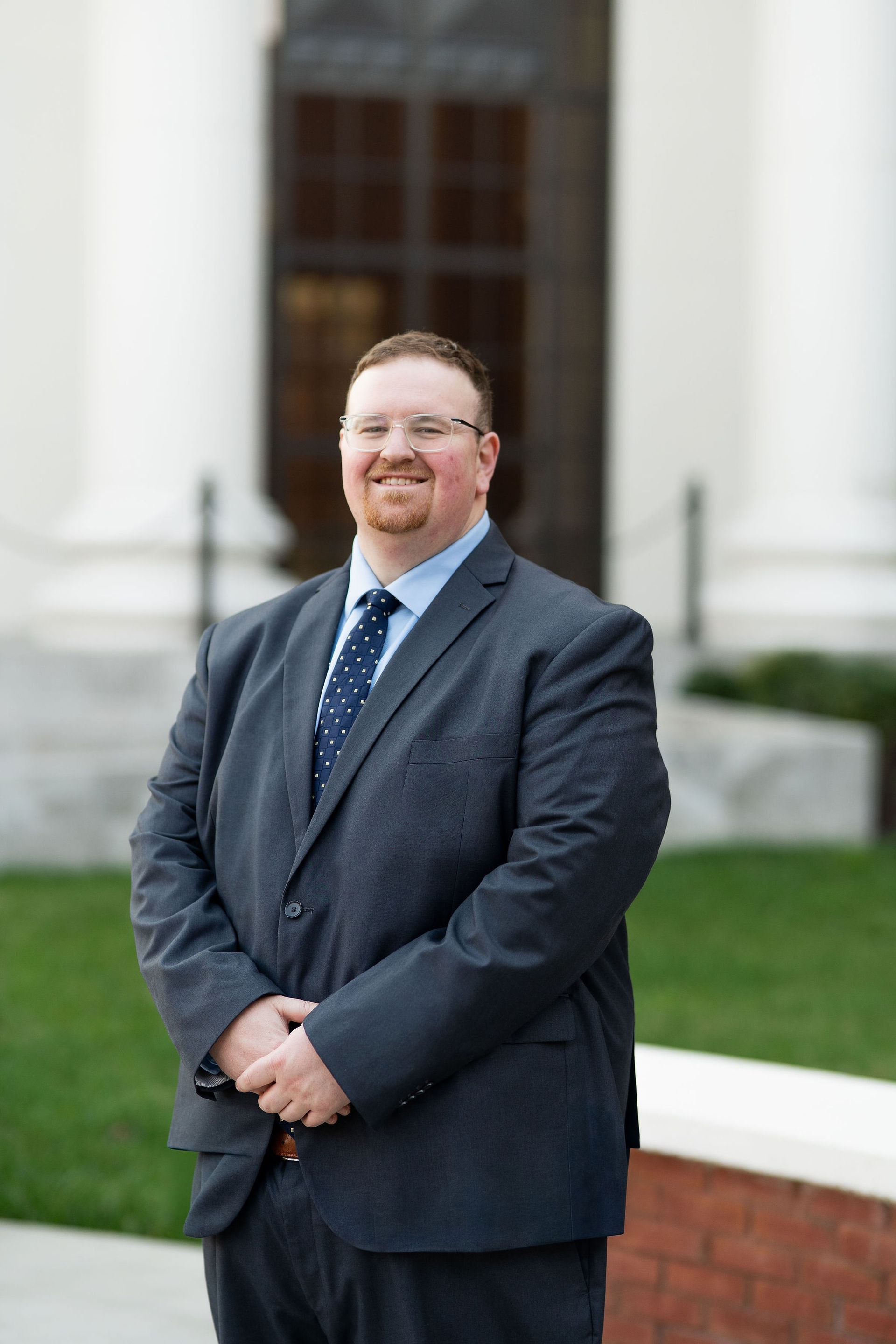 Man in a dark suit standing outdoors in front of a building with white columns