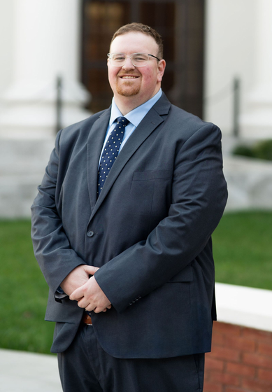 Smiling man in a dark suit standing outdoors near a building entrance