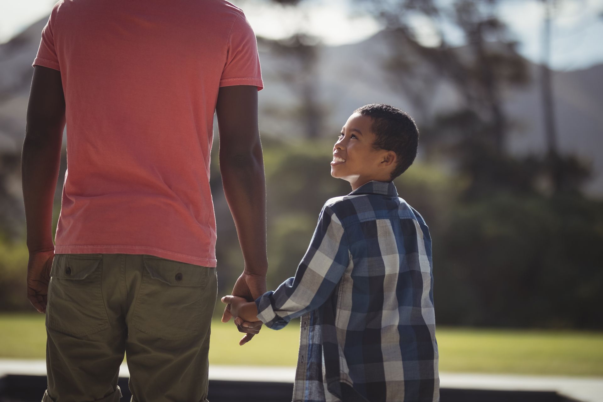 Adult and child holding hands outdoors in a park, walking together in sunlight