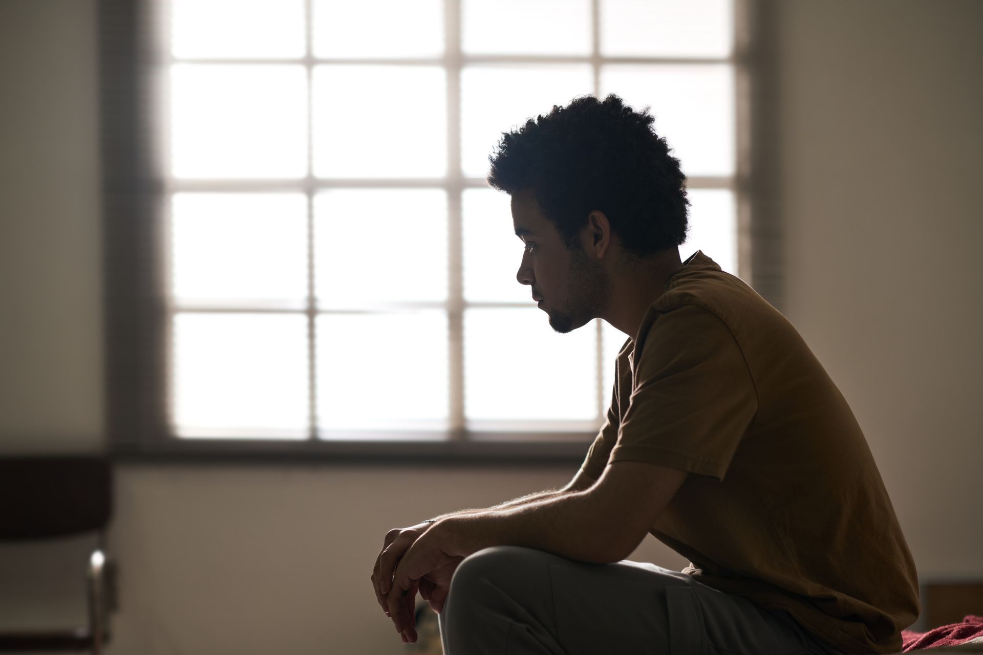 Silhouetted person sitting by a bright window in a dim room