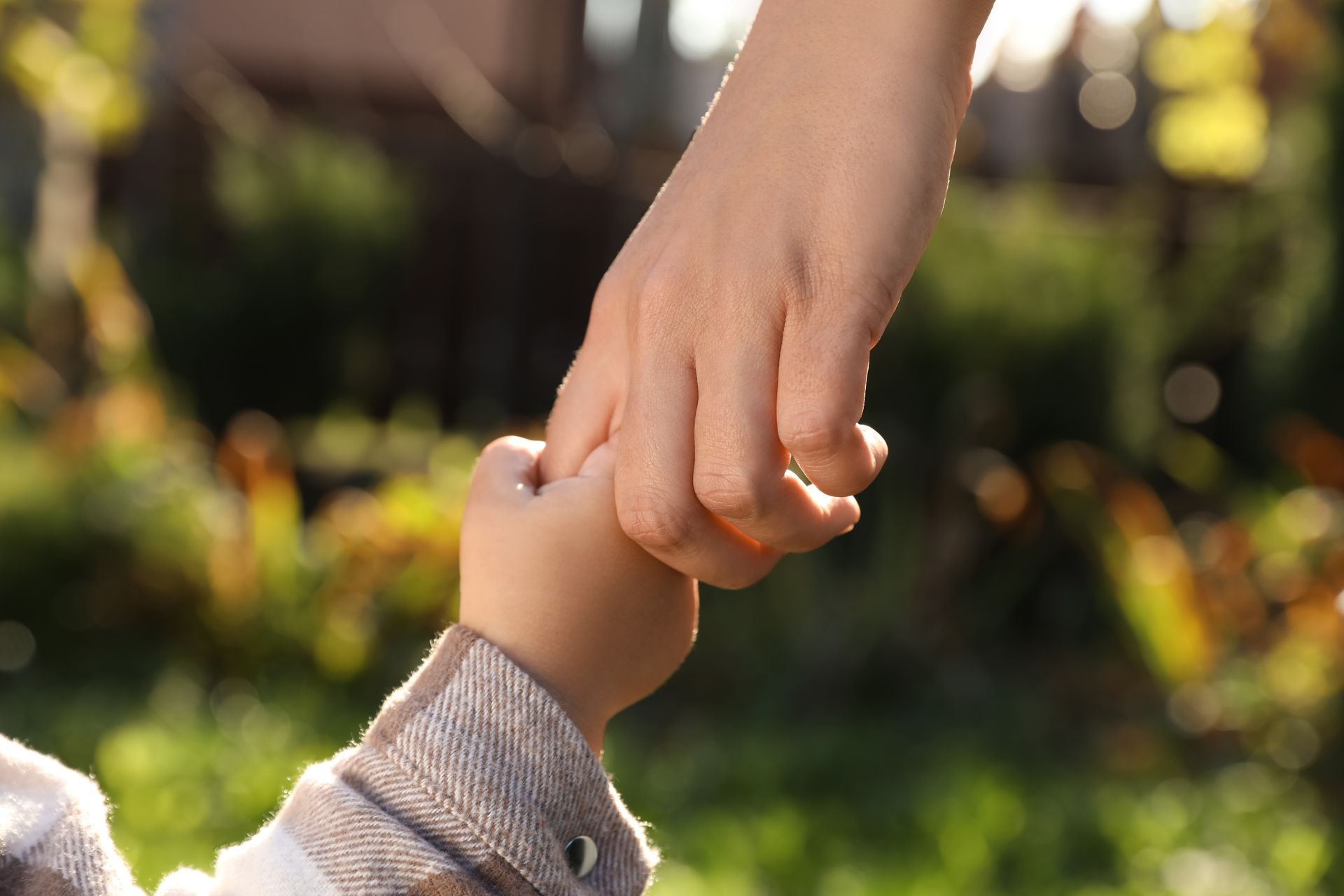 Adult and child holding hands in a sunlit garden