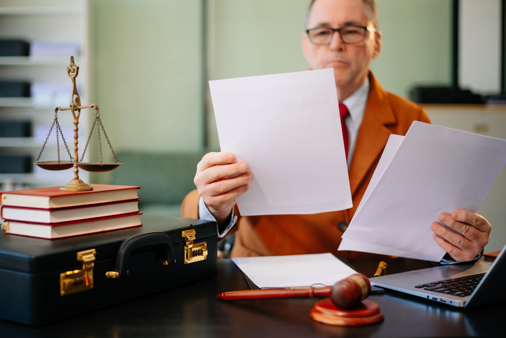 Lawyer reviewing documents at a desk with scales, briefcase, and laptop