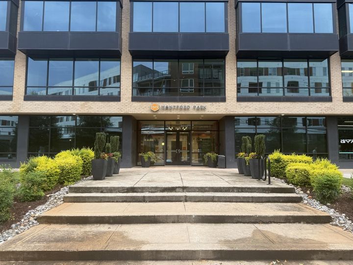 Modern office building entrance with steps, glass facade, and landscaped planters