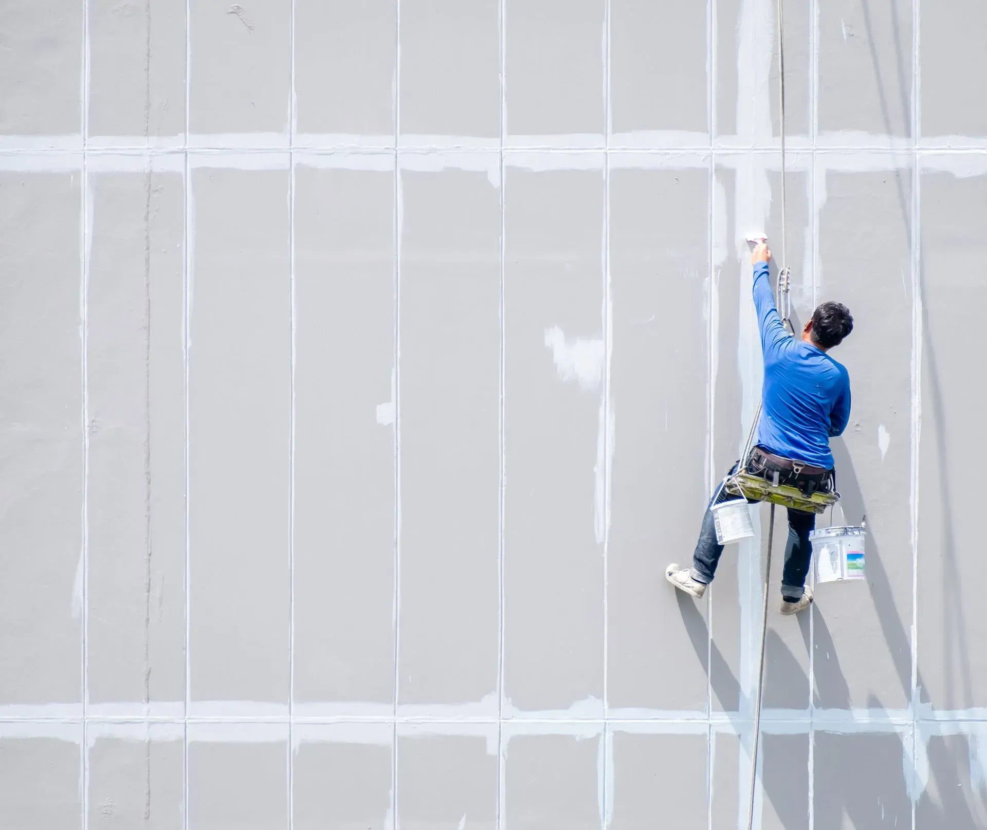 A man is painting a building from a rope.