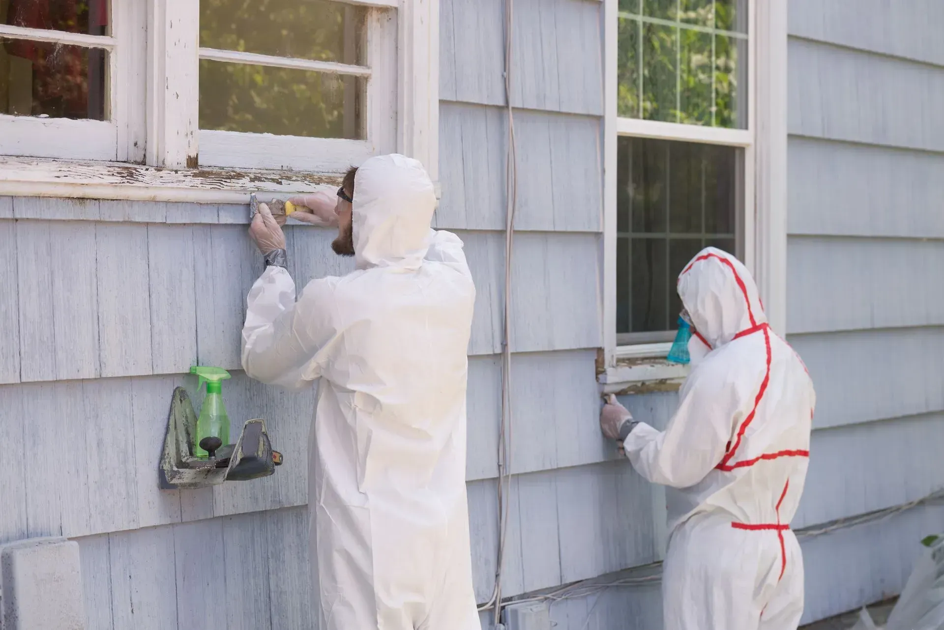 Two people in protective suits are working on the side of a house.