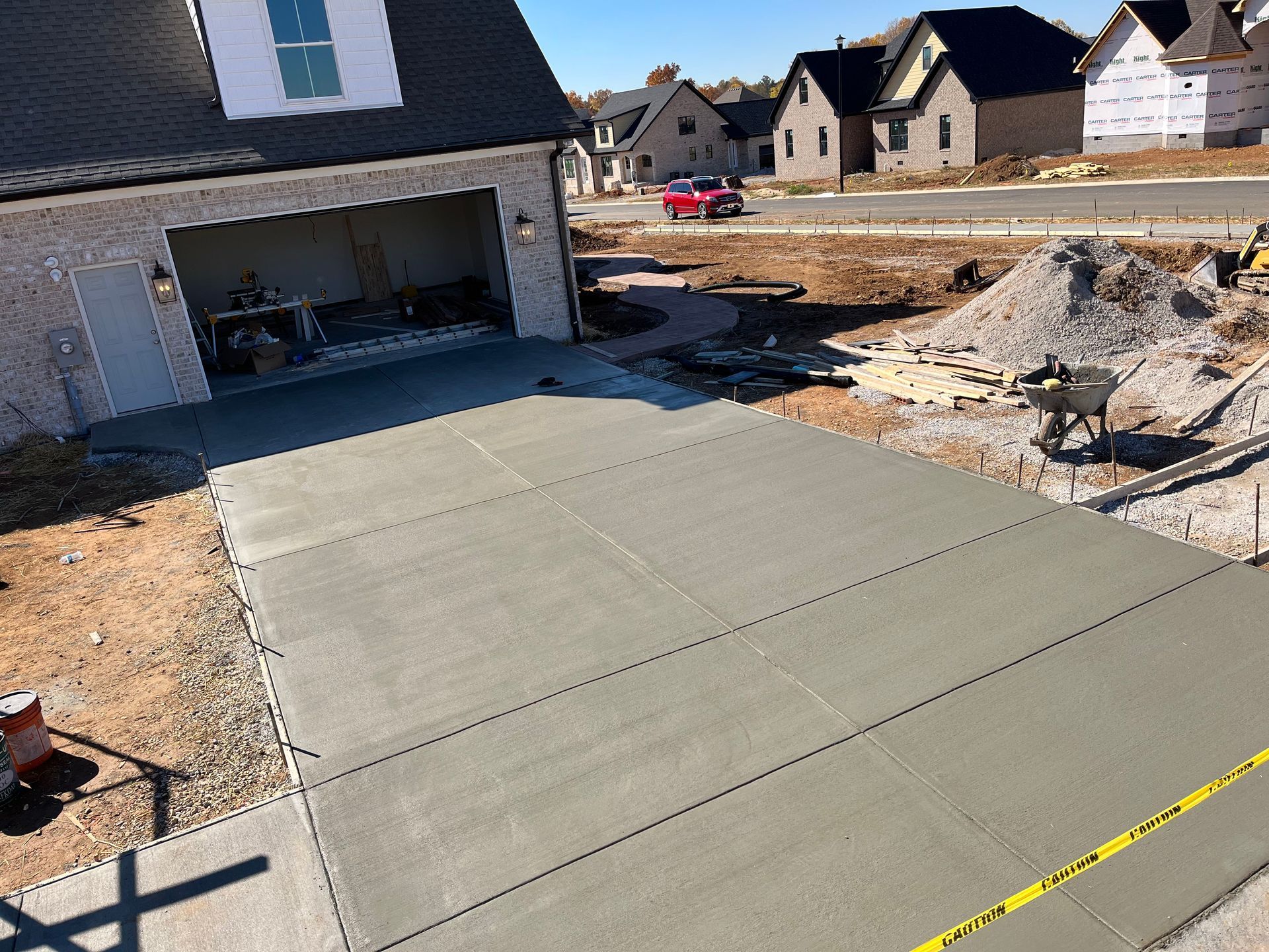 Fresh concrete driveway beside a house under construction, with rock landscaping and neighboring homes in view