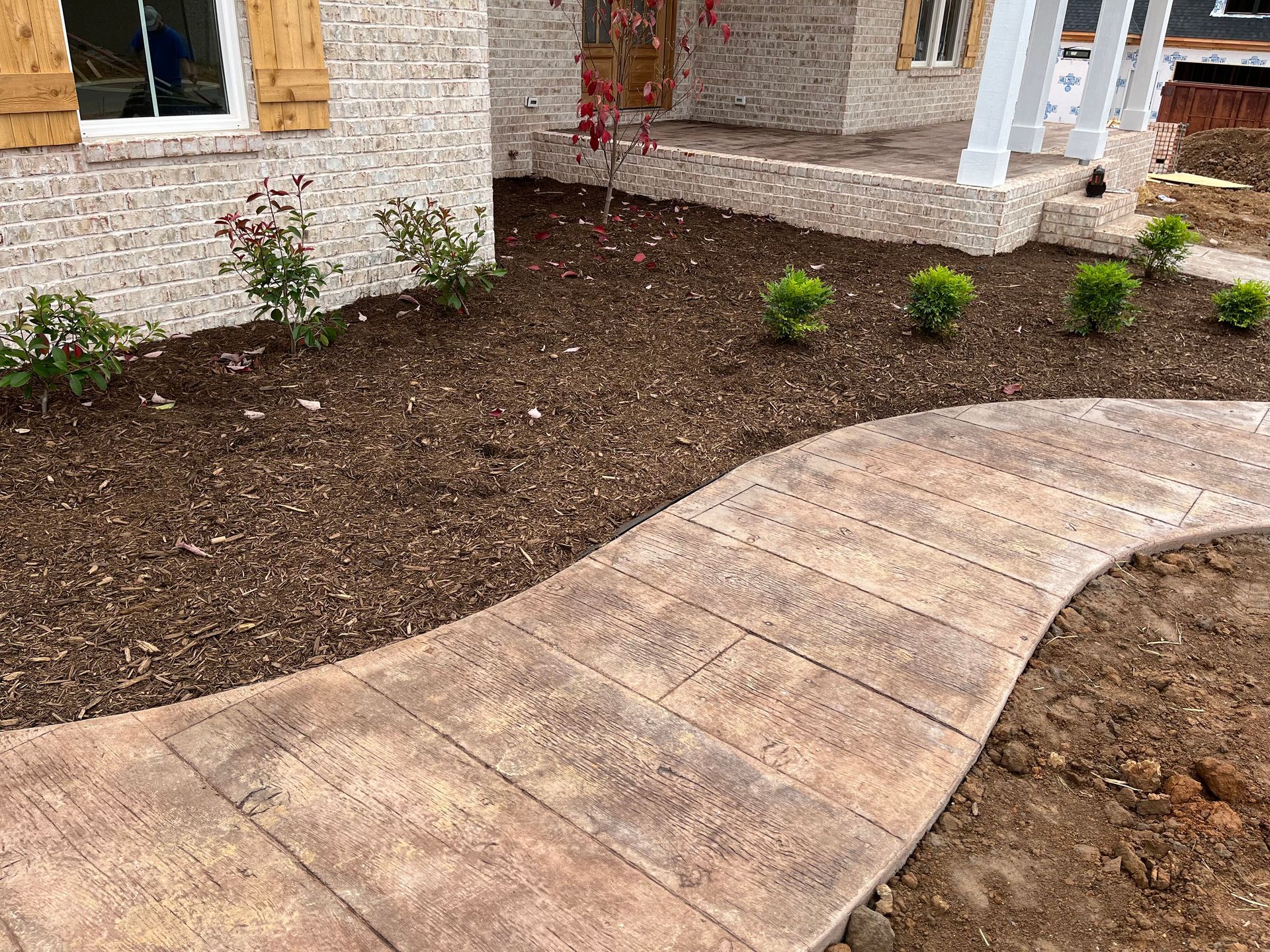 Curved stone walkway beside a house with freshly mulched landscaping and small shrubs