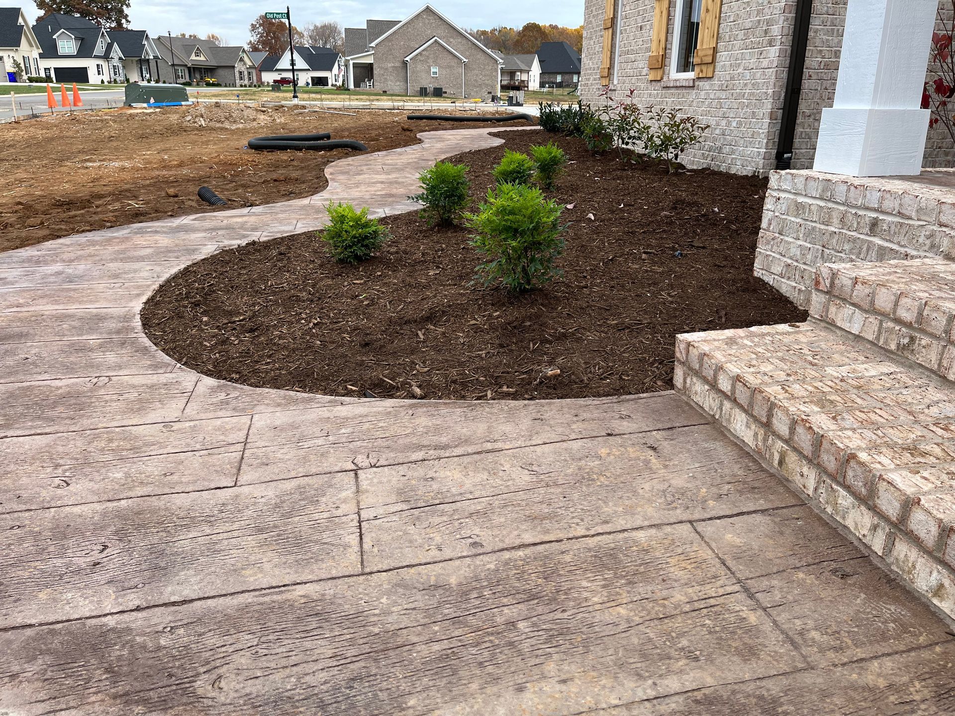 New concrete patio beside brick steps and a mulched front yard with young shrubs