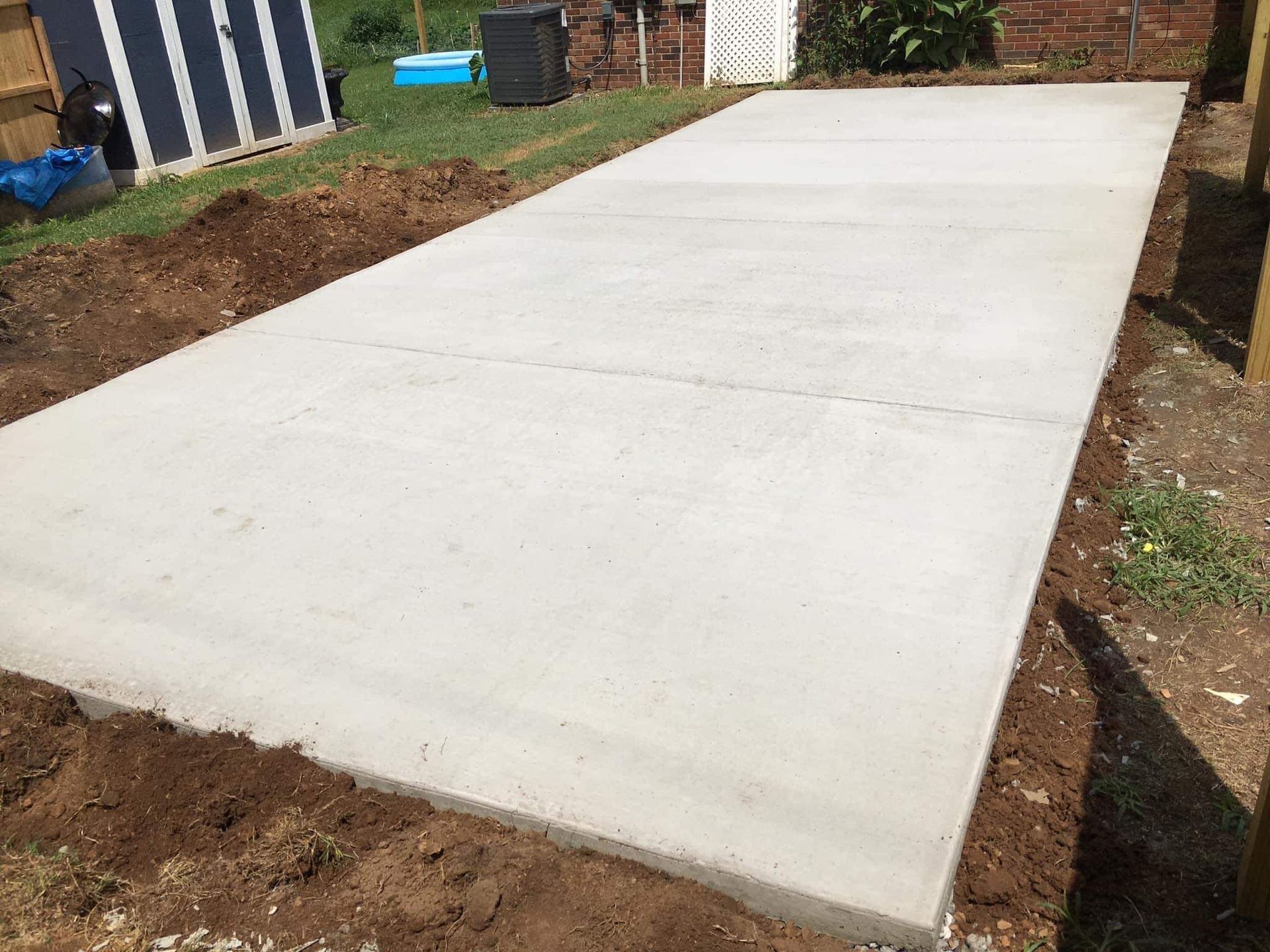 Newly poured concrete driveway beside a house, bordered by dirt and grass