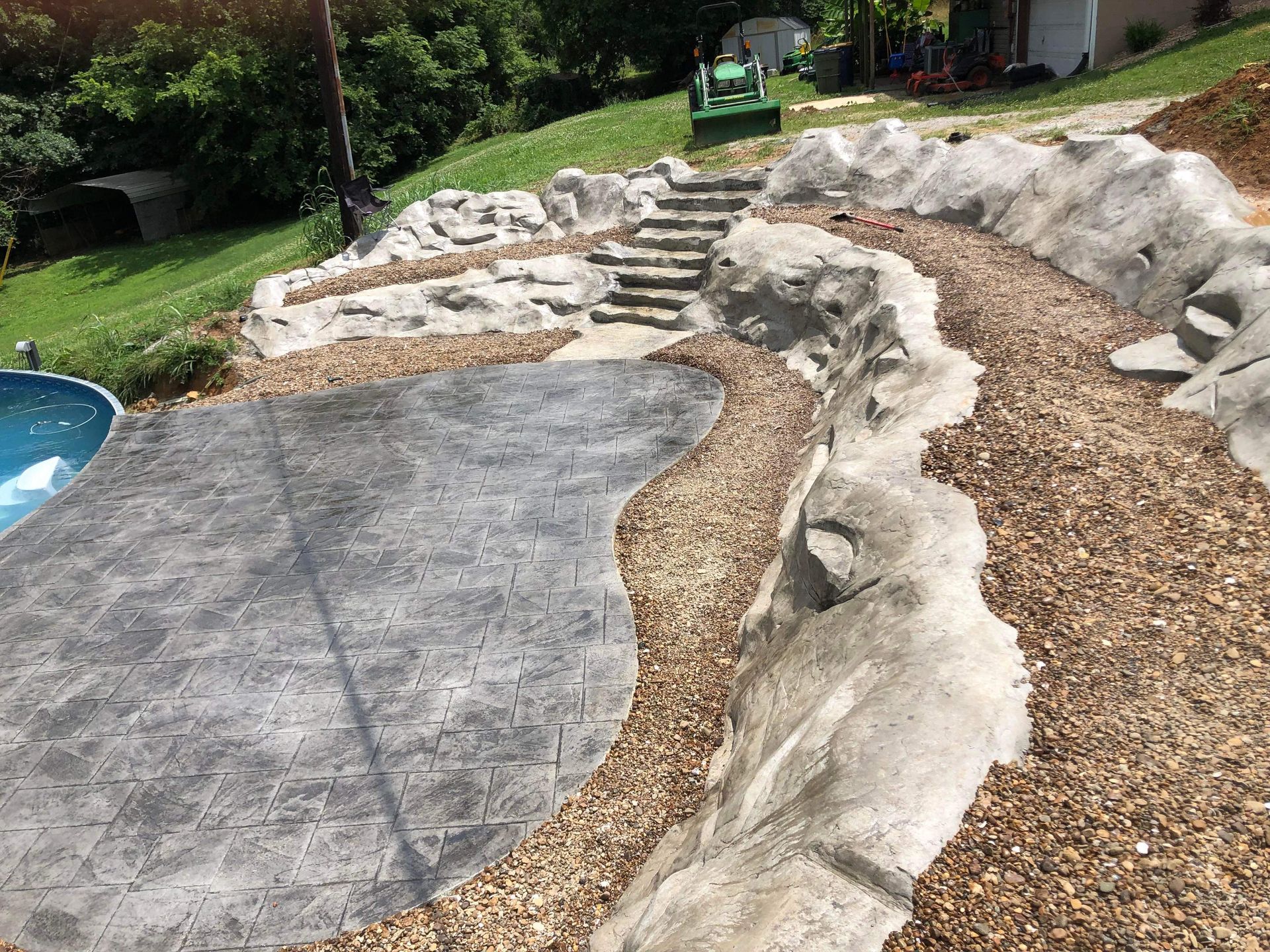 Backyard landscape with stone steps, gravel path, and a concrete patio beside a pool