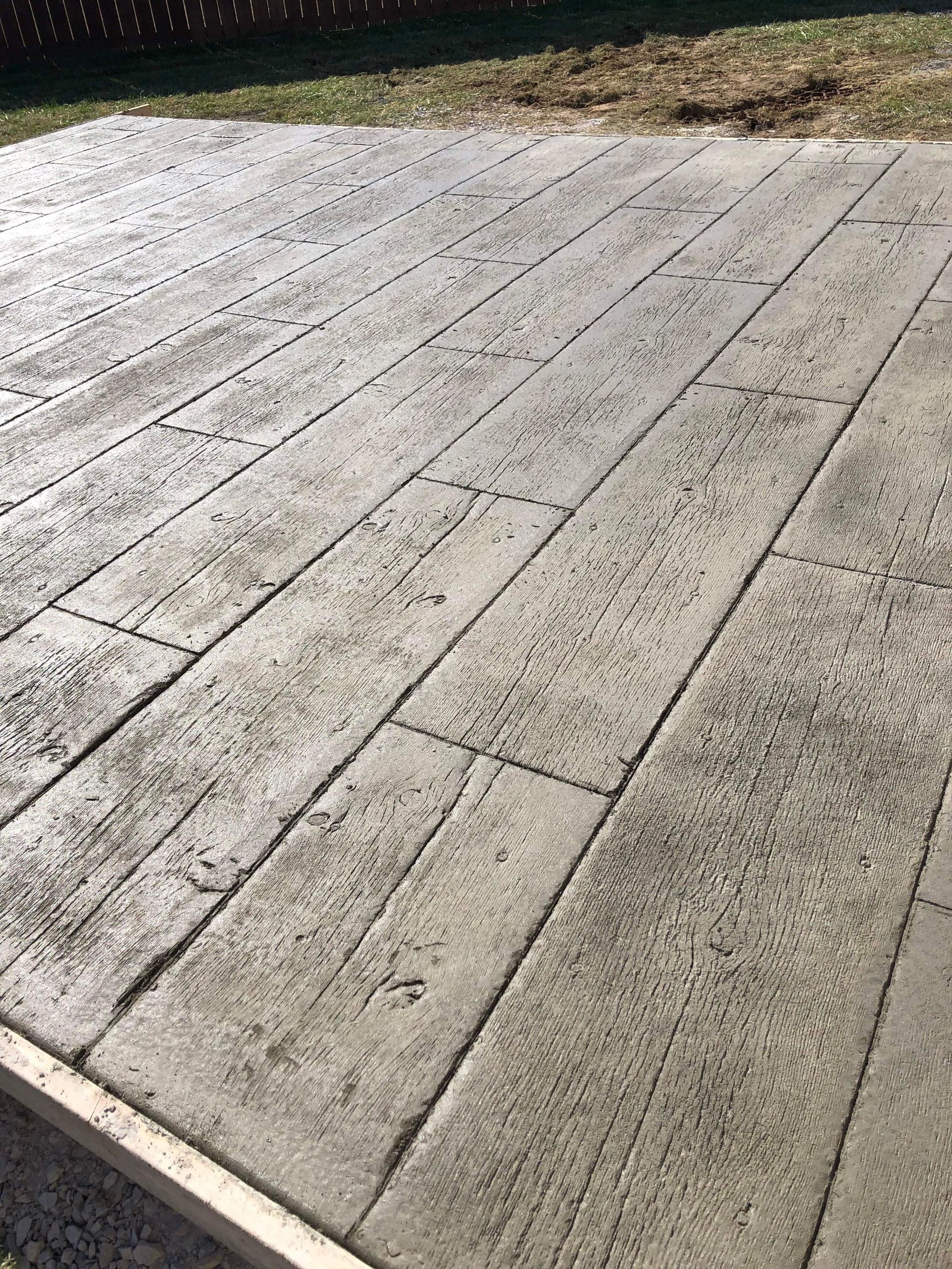 Weathered concrete patio or deck with long plank-like seams, viewed in sunlight.