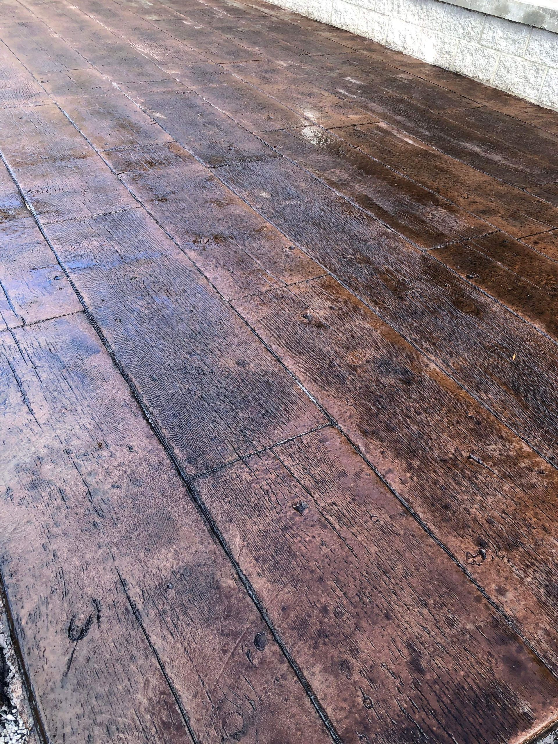 Wet, weathered concrete pavement with dark tire-like streaks and reflections of light