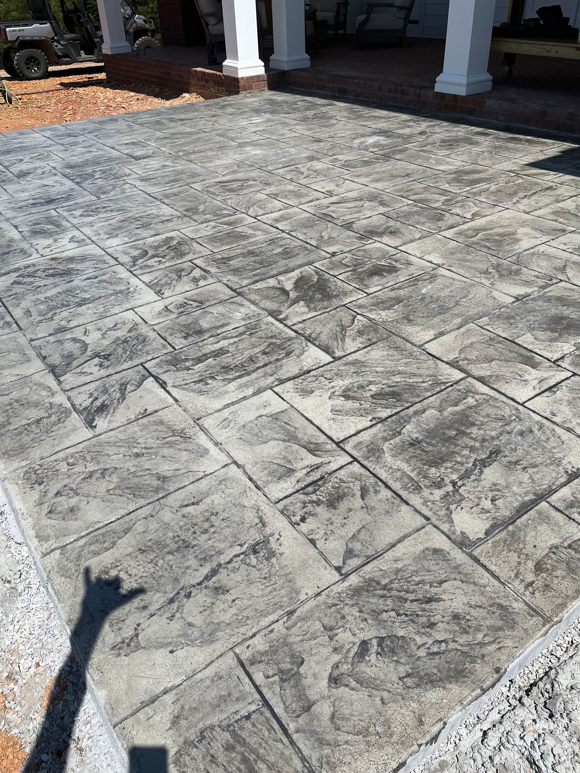 Stamped concrete driveway leading to a covered porch with white columns and a shadow in the foreground