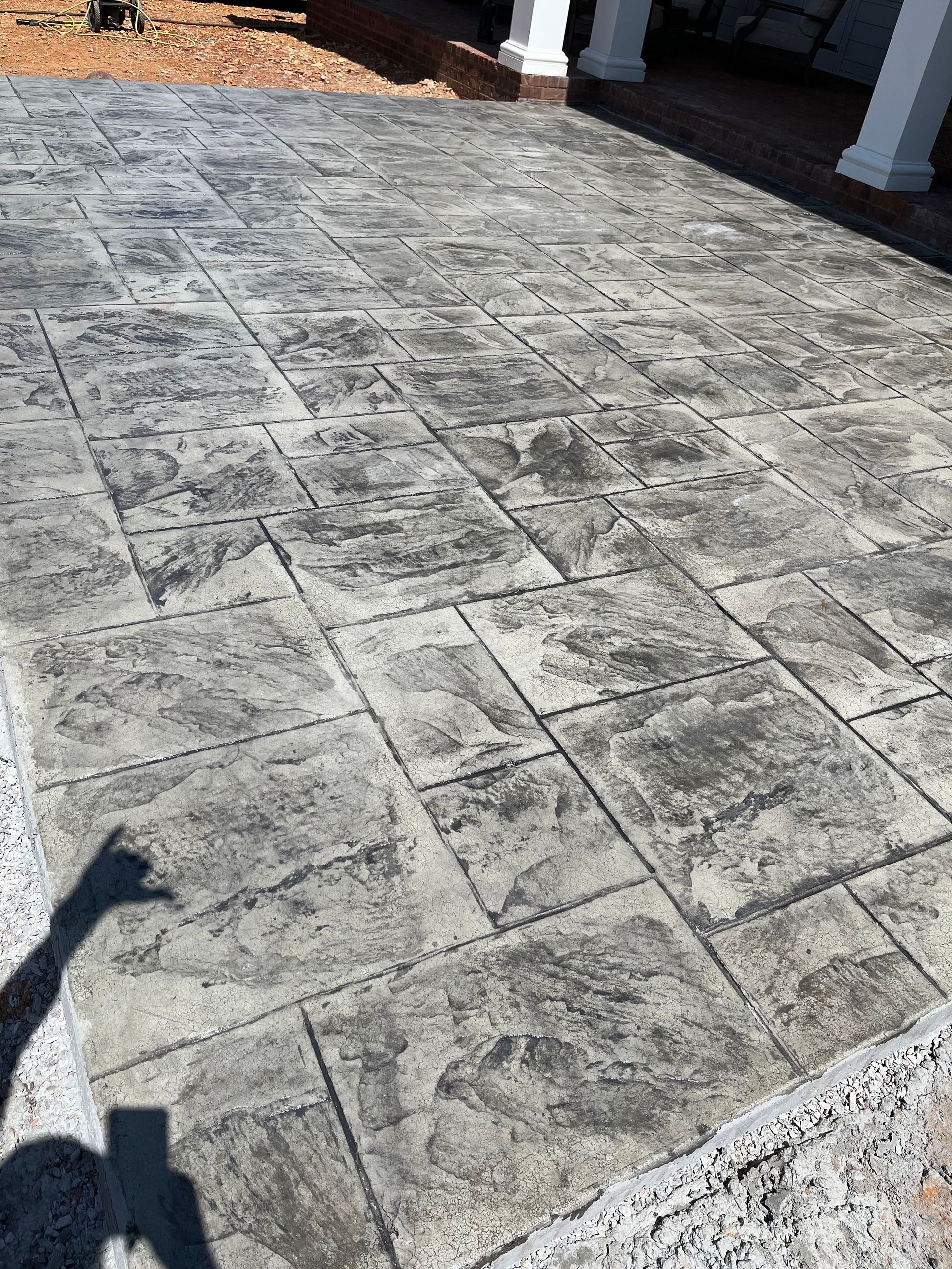 Stamped concrete patio with a light gray stone pattern and a person’s shadow in the lower left.