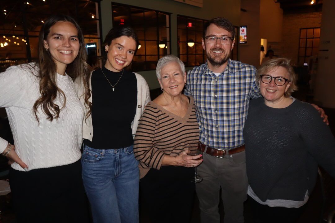 Five people standing together indoors, smiling at the camera in a warmly lit restaurant.