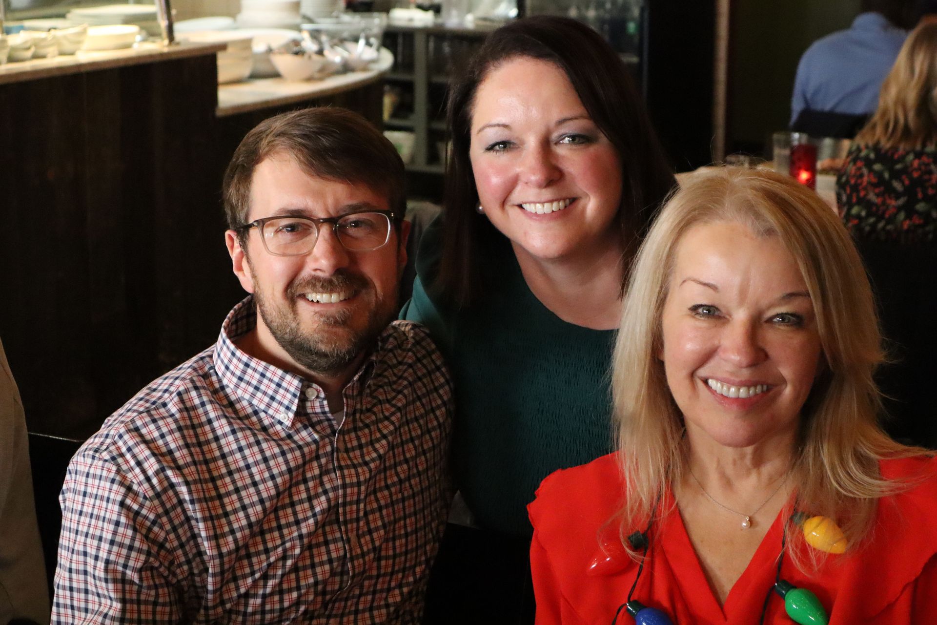 Three people smiling together at a restaurant table, with two cups visible behind them.