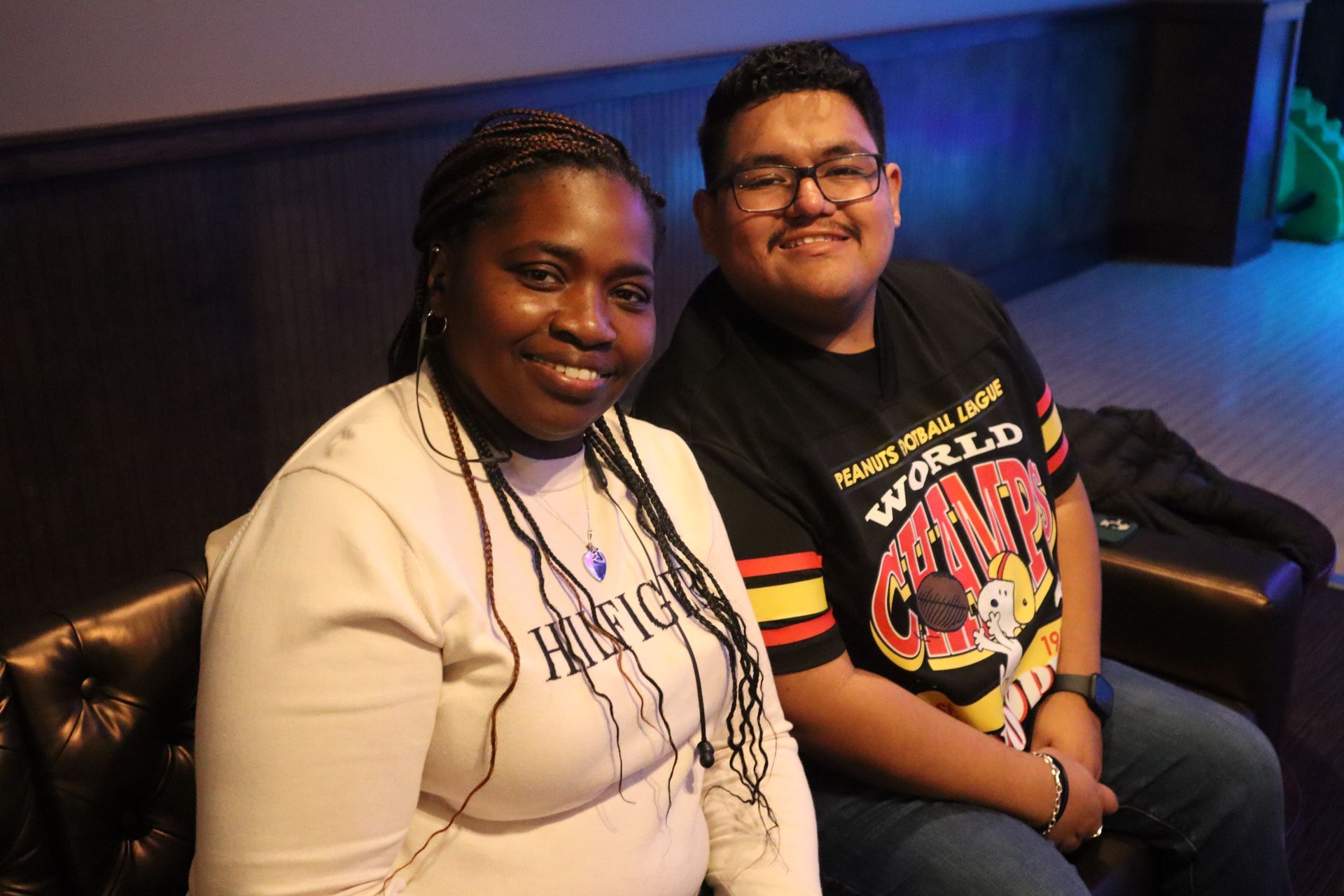 Two people sitting on a couch, smiling in a dimly lit lounge.