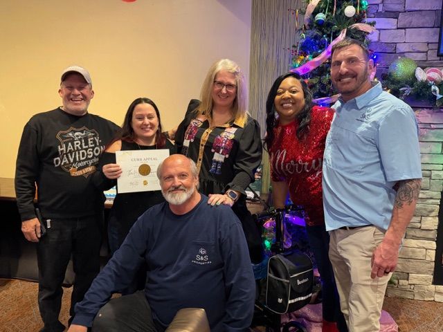 Group posing with a certificate beside a Christmas tree in a lobby.
